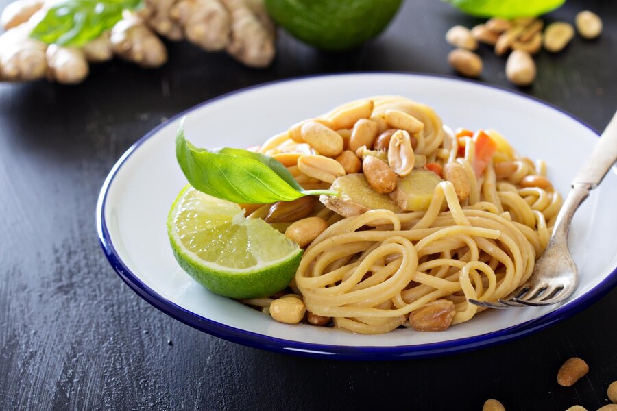 A plate of vegan Thai peanut noodles garnished with peanuts, lime, and ginger, showcasing a vibrant and appetizing dish.