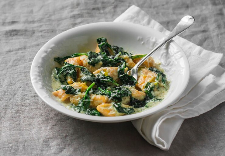 A bowl of creamy vegan tortellini soup featuring spinach and chicken, accompanied by a spoon, perfect for Valentine's Day.