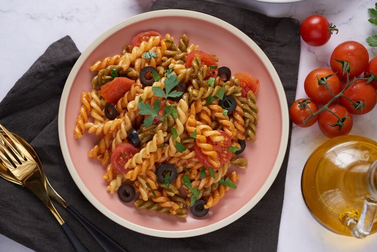 A vibrant vegan tomato fusilli pasta dish adorned with fresh tomatoes and black olives, perfect for Valentine's Day.