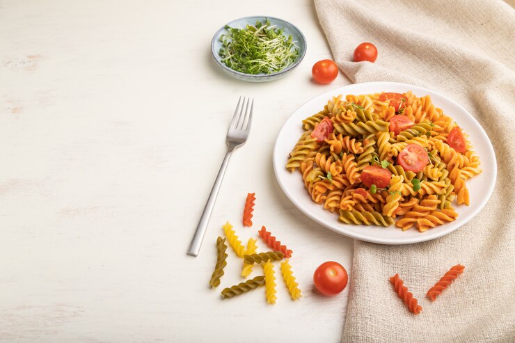 A top view of vegan tomato fusilli pasta with vegetables, elegantly presented on a white table for Valentine's Day.