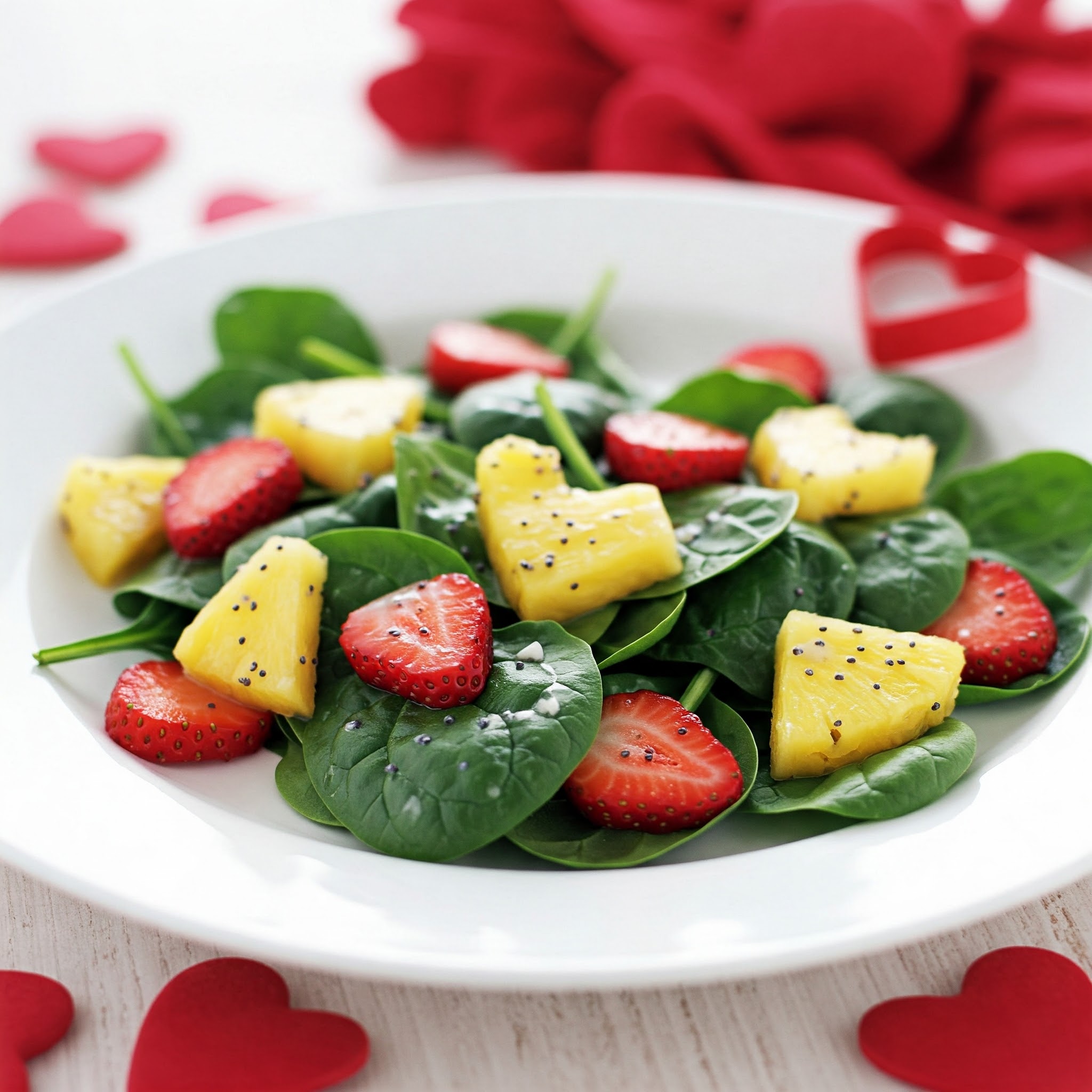 A vibrant plate featuring Valentine's Spinach Salad topped with fresh strawberries and pineapple chunks.