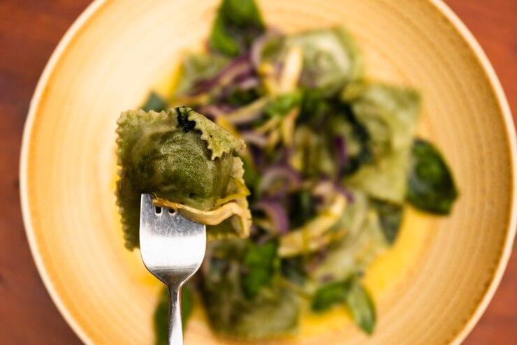 A fork lifts a plate of vegan kale and sweet potato ravioli, garnished with fresh spinach, perfect for Valentine's Day.