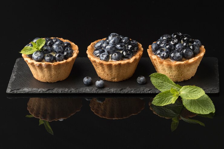 Three blueberry tartlets elegantly arranged on a black slate, embodying the sweet romance of Valentine's Day.