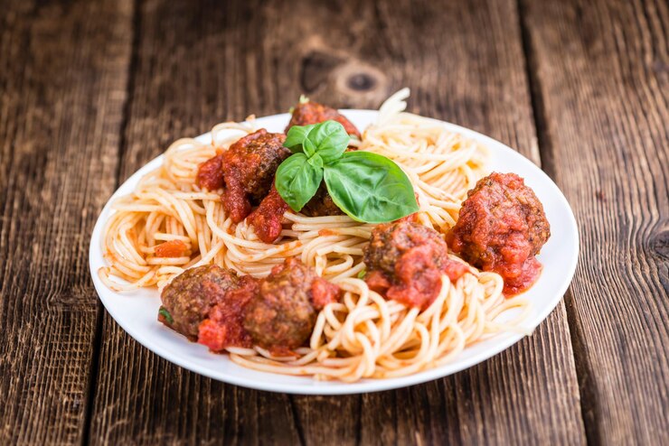 A plate of vegan spaghetti topped with lentil balls and tomato sauce, set on a wooden table for a romantic dinner.