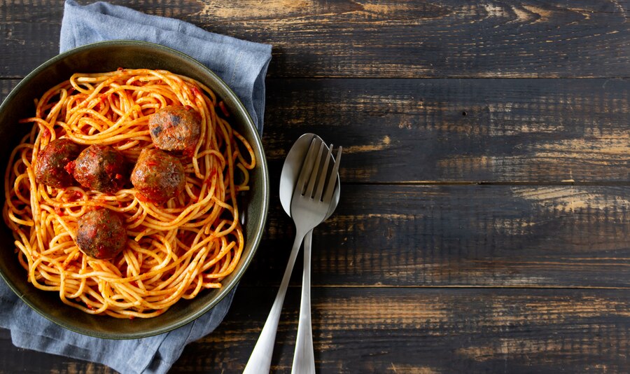 A bowl of vegan spaghetti with lentil balls, elegantly presented on a rustic wooden table for a romantic Valentine's dinner.