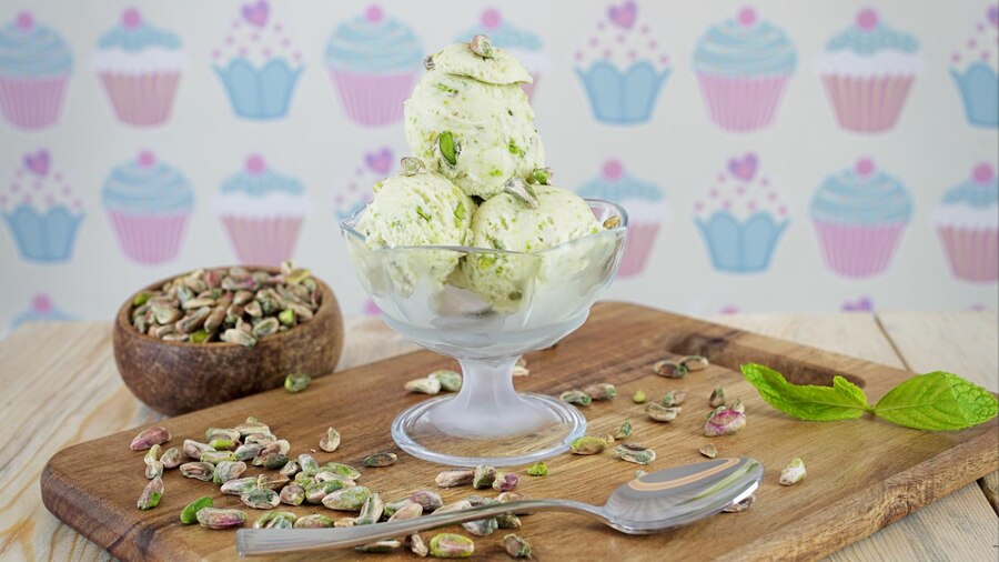 A bowl of vegan pistachio ice cream topped with pistachios and fresh mint leaves, showcasing a vibrant green color.