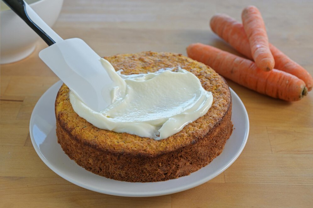Vegan carrot cake topped with smooth cream cheese frosting, showcasing a moist texture and vibrant orange color.