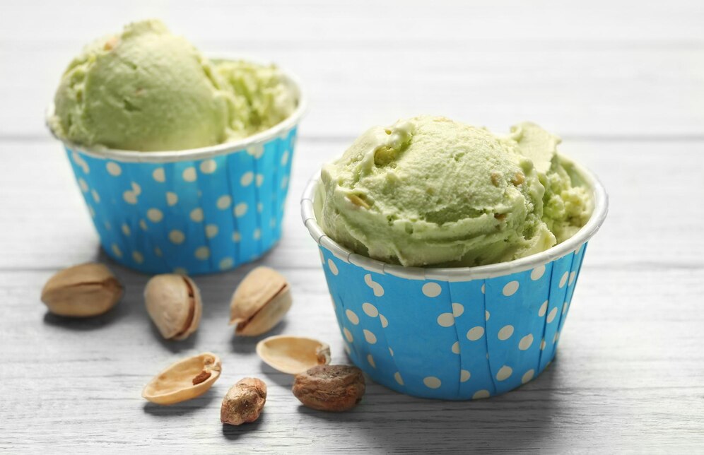 Two cups of green pistachio ice cream topped with crushed pistachios, showcasing a vibrant and creamy dessert.