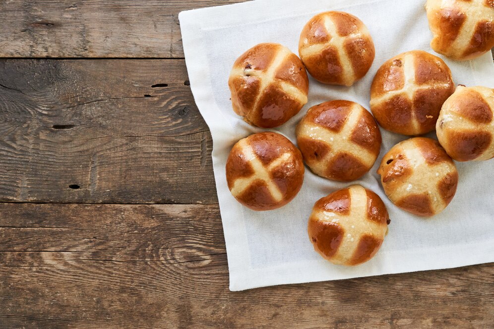 Vegan hot cross buns arranged on a napkin atop a wooden table, perfect for an Easter brunch celebration.
