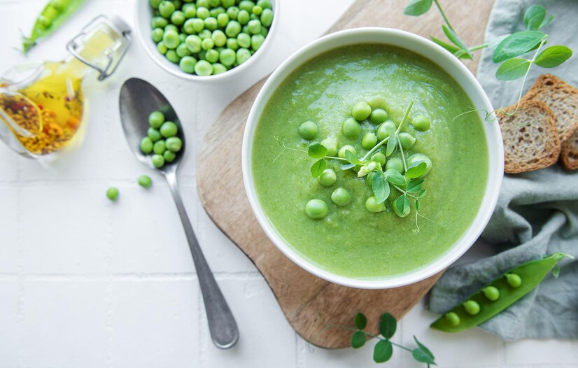 Green pea and mint soup served with bread on a white background, showcasing a fresh spring recipe.