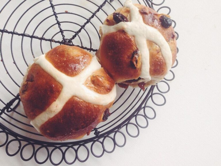 A close-up of golden-brown vegan hot cross buns cooling on a wire rack, ideal for Easter brunch.