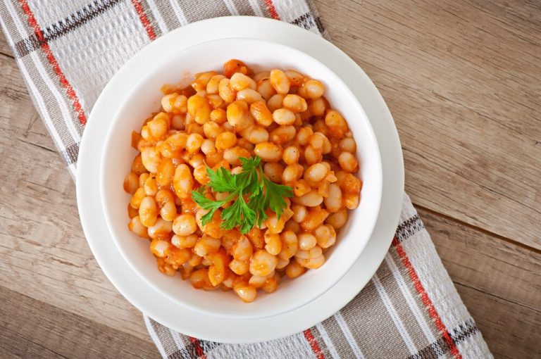 A wooden table holds a bowl of Marry Me Butter Beans topped with fresh parsley, showcasing a popular TikTok recipe.