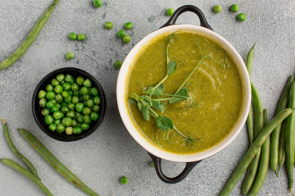 Green pea soup garnished with fresh herbs and green beans, set against a gray background, representing a spring recipe.