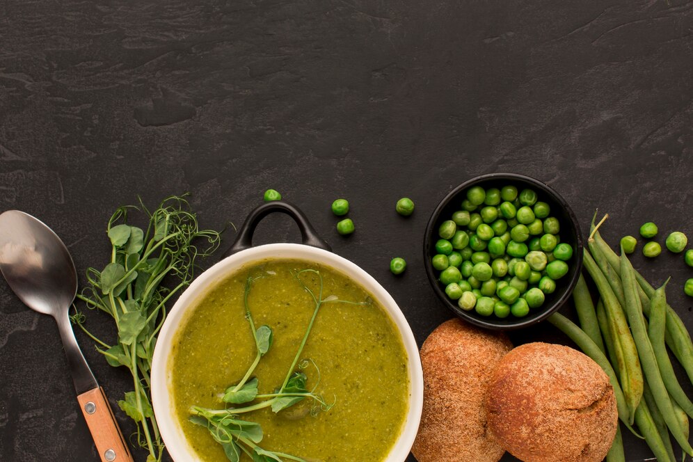 Green pea and mint soup with bread and spoons on a black background, showcasing a fresh spring recipe.