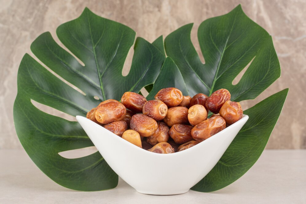 A bowl of dates with a green leaf on a wooden table, highlighting a vegan recipe for trending pistachio-stuffed dates