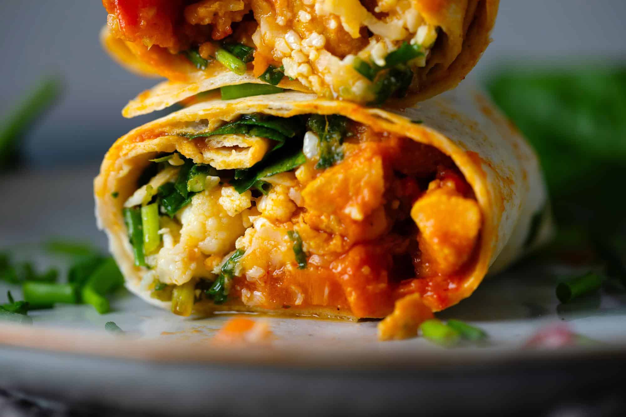 Close-up of a sliced vegan wrap filled with vegetables, greens, and tomato-based sauce on a plate