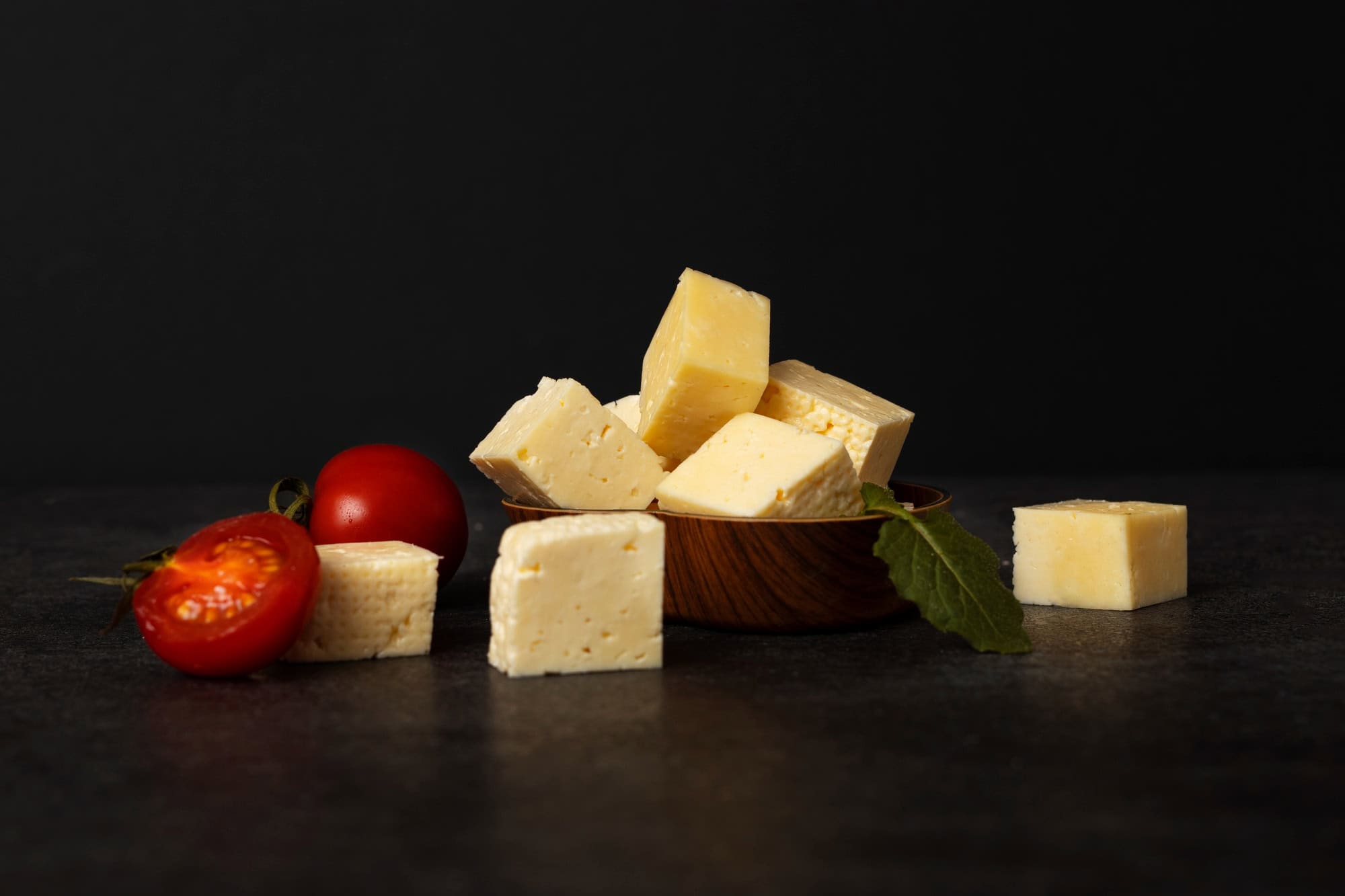 Cubes of cheese arranged beside cherry tomatoes on a dark background with minimalist rustic styling