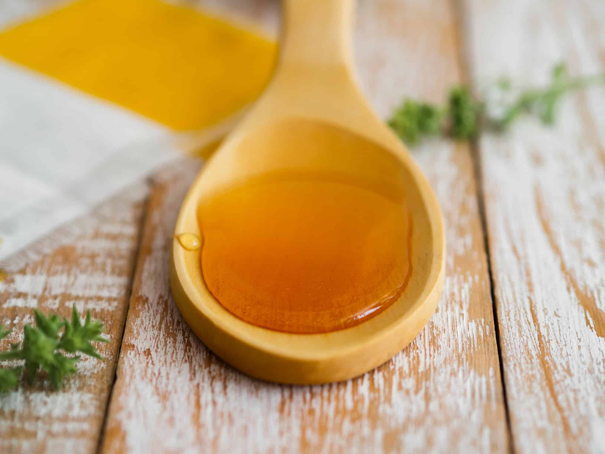 Golden vegan butterscotch syrup on a wooden spoon, sitting on a rustic wooden table with herbs in the background for vegan butterbeer recipe.