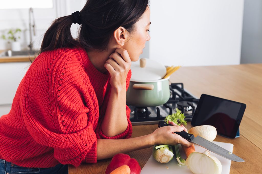 Home cook preparing fresh vegetables on a kitchen counter while following a recipe, representing mindful plant-based comfort cooking